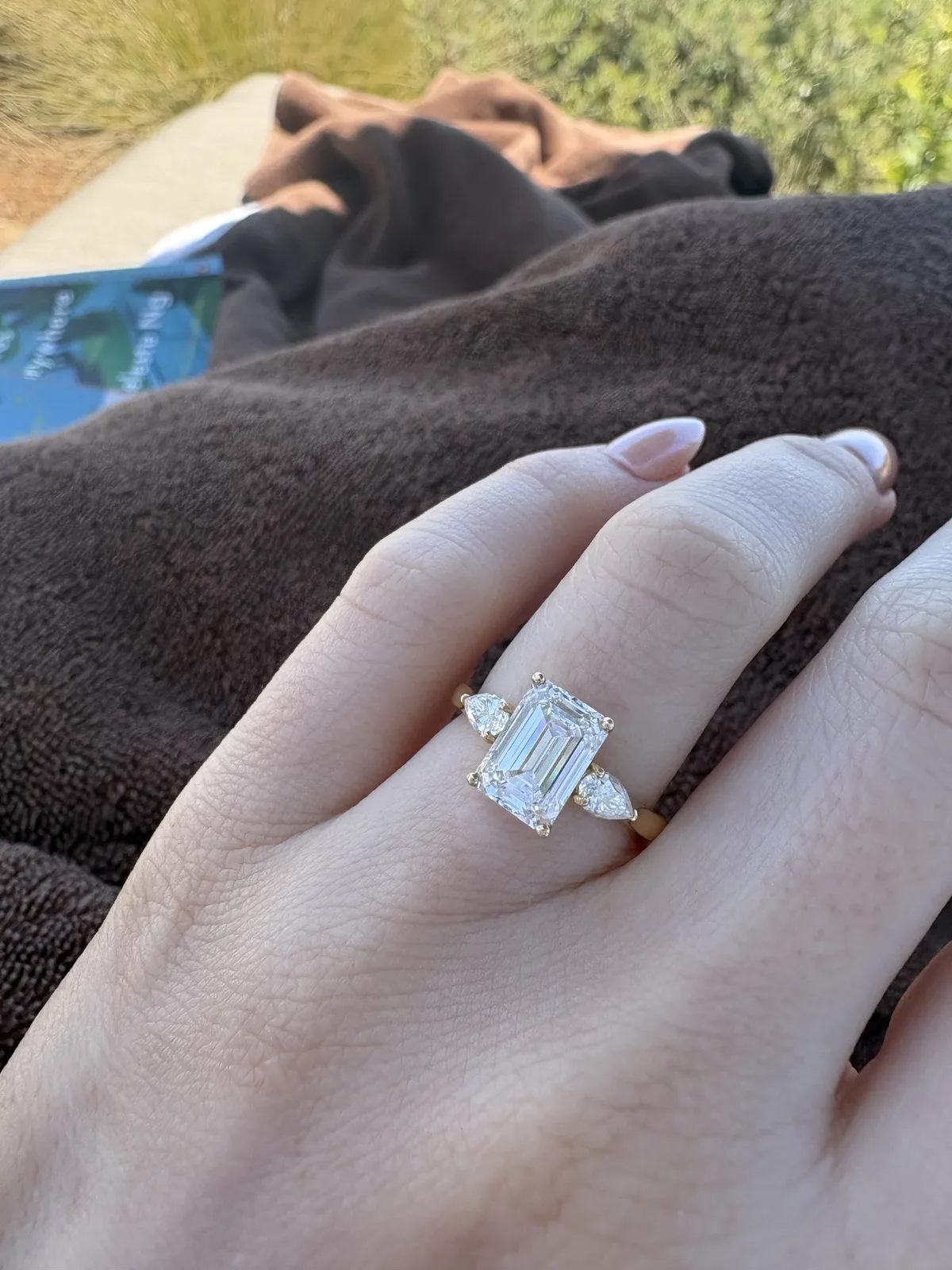 Custom emerald cut three-stone engagement ring on hand in golden light, designed at Haejin Jewelry NYC