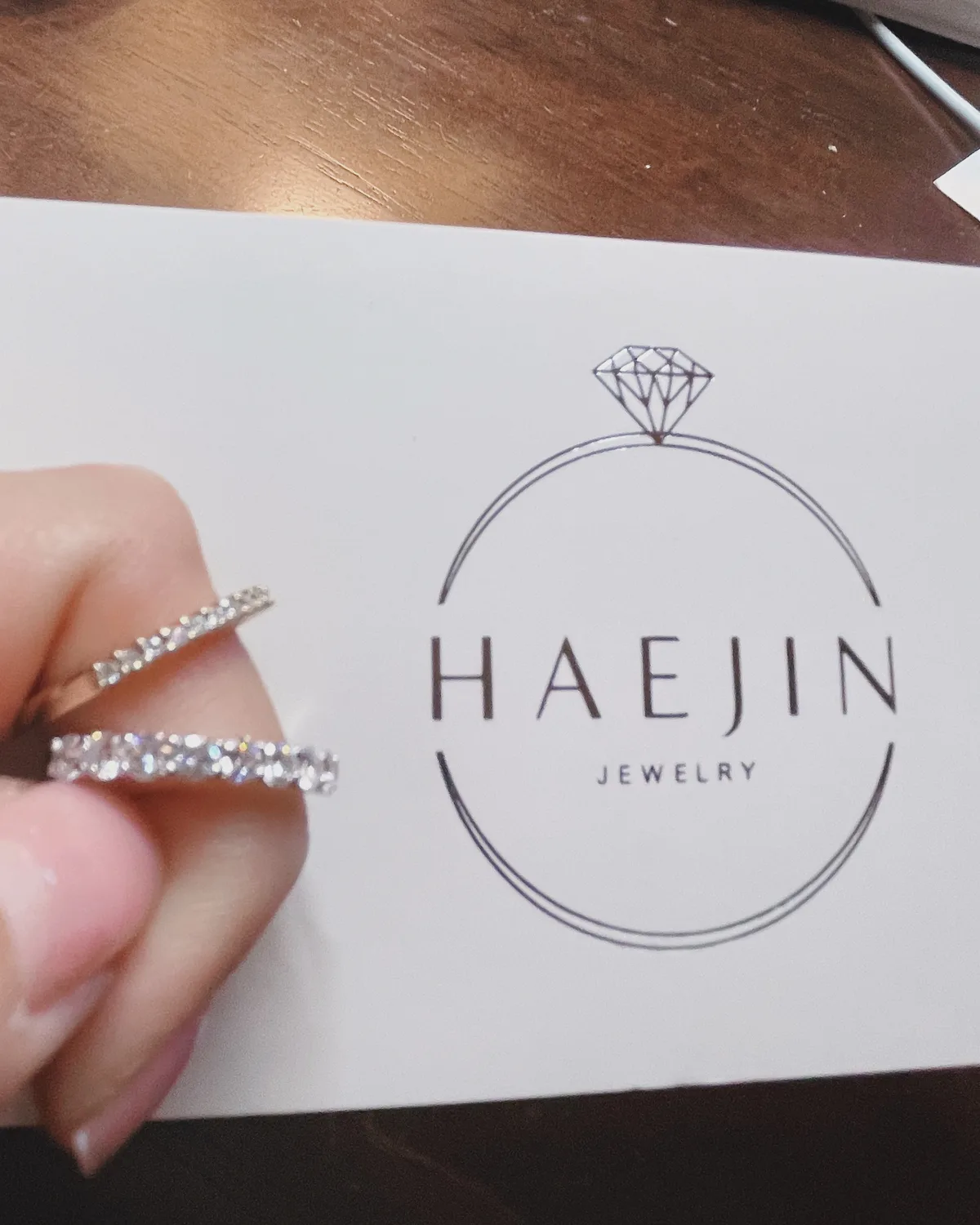 Diamond crossover wedding band held next to Haejin Jewelry Brooklyn logo card