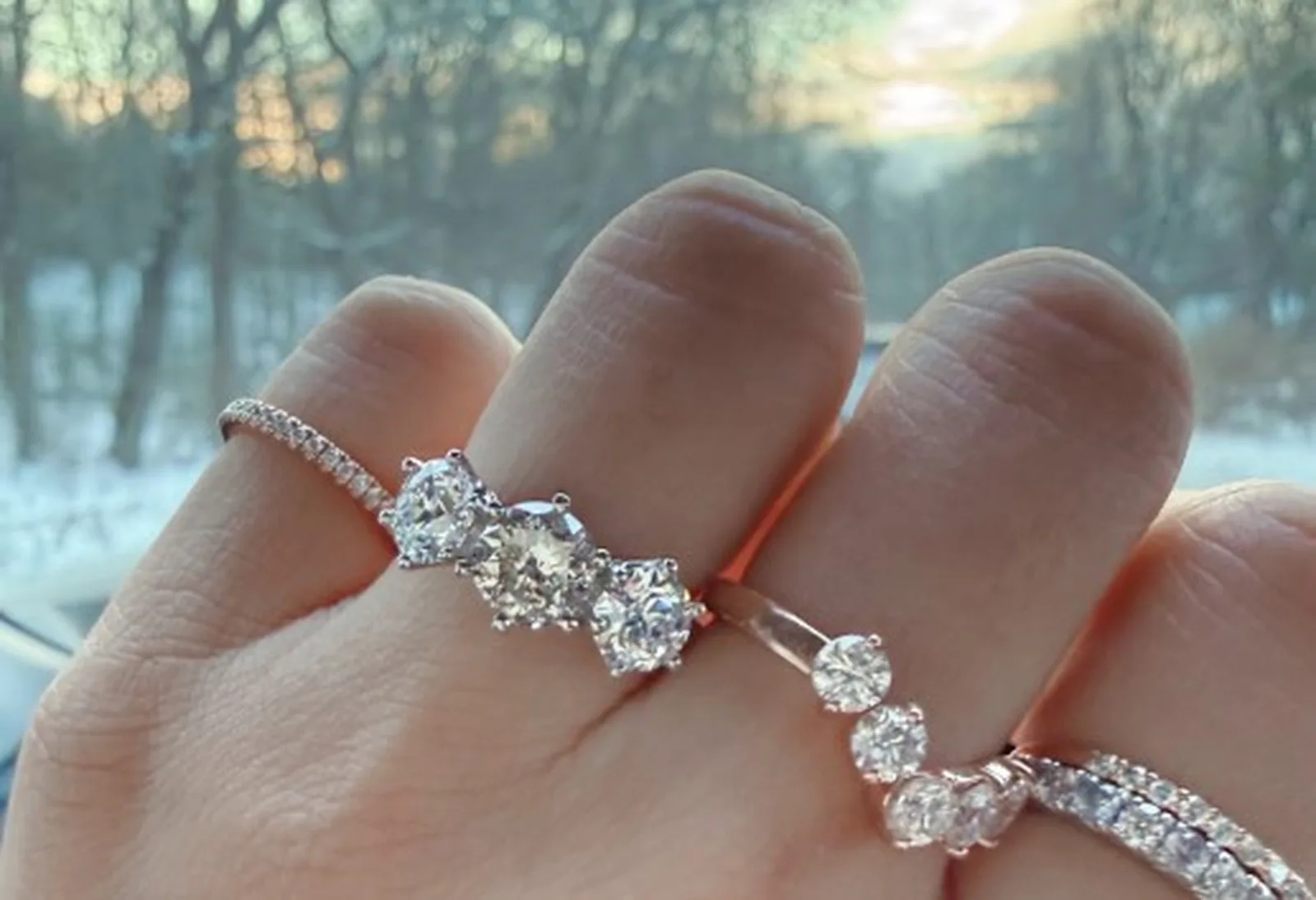 Three-stone diamond engagement ring paired with graduated diamond band on hand in golden-hour winter light, Haejin Jewelry Brooklyn