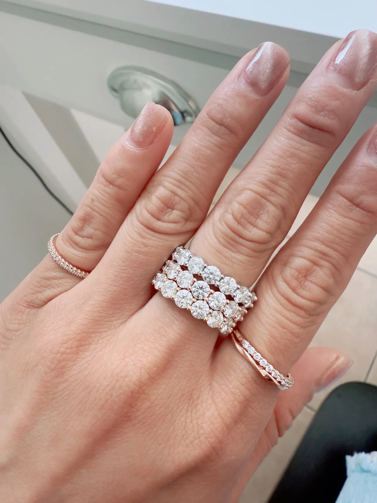 Five diamond eternity bands stacked in rose gold showing large stones and thin pave together on hand, Haejin Jewelry Brooklyn