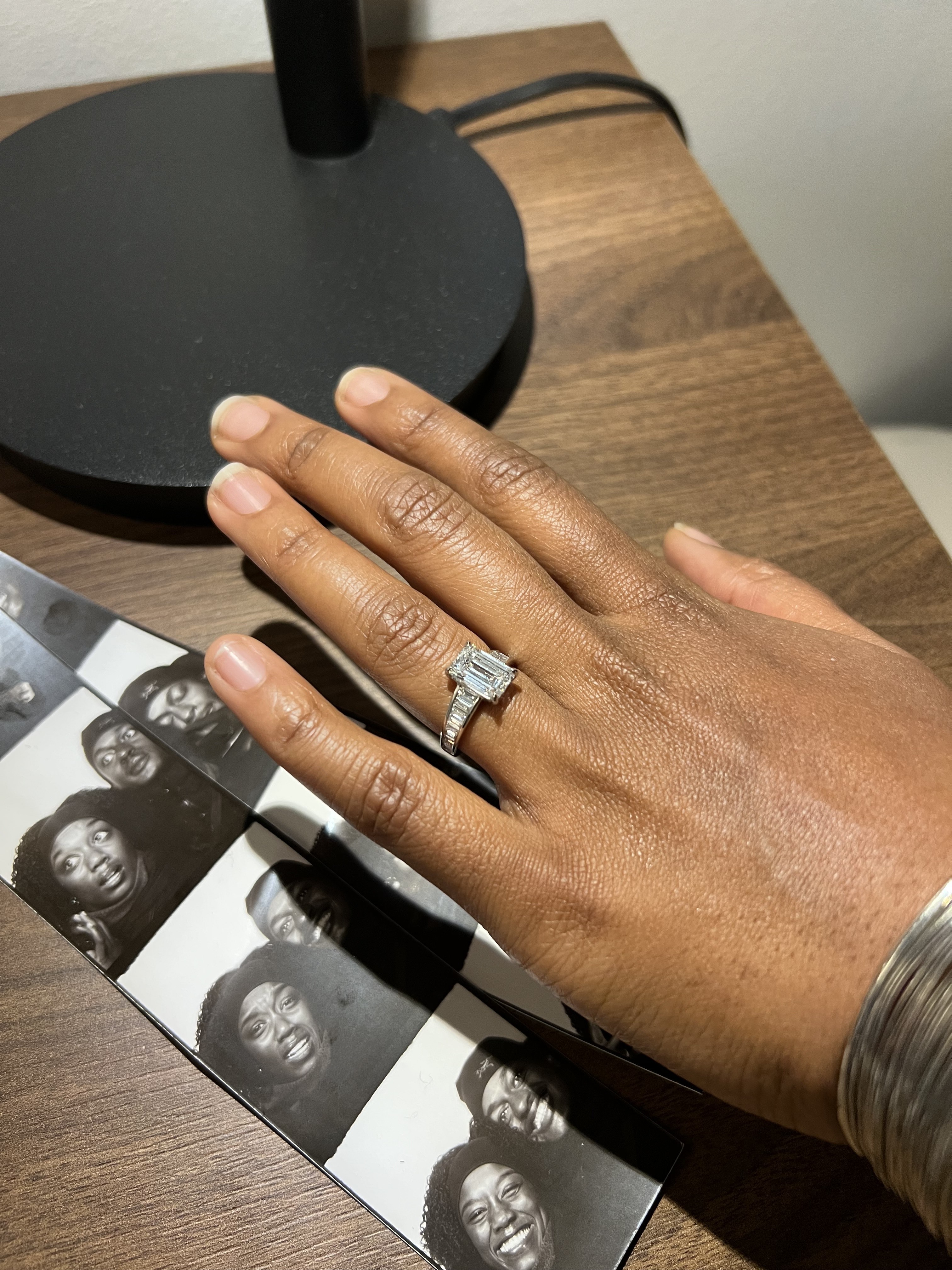Custom three-stone emerald cut engagement ring on hand next to photo booth pictures of the couple, designed at Haejin Jewelry Brooklyn