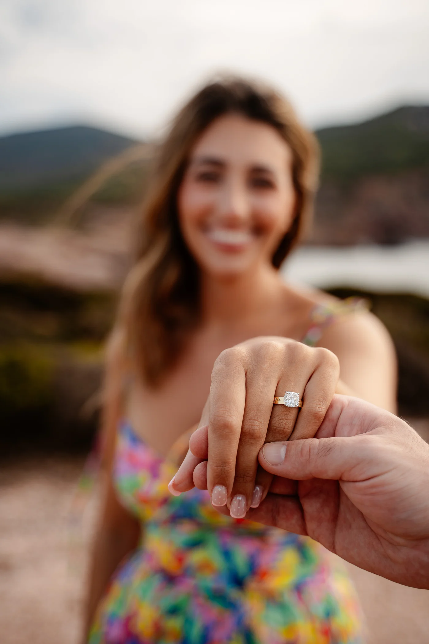 Newly engaged woman smiling behind her hand, showing a cushion cut yellow gold engagement ring from Haejin Jewelry on the Sardinian coast
