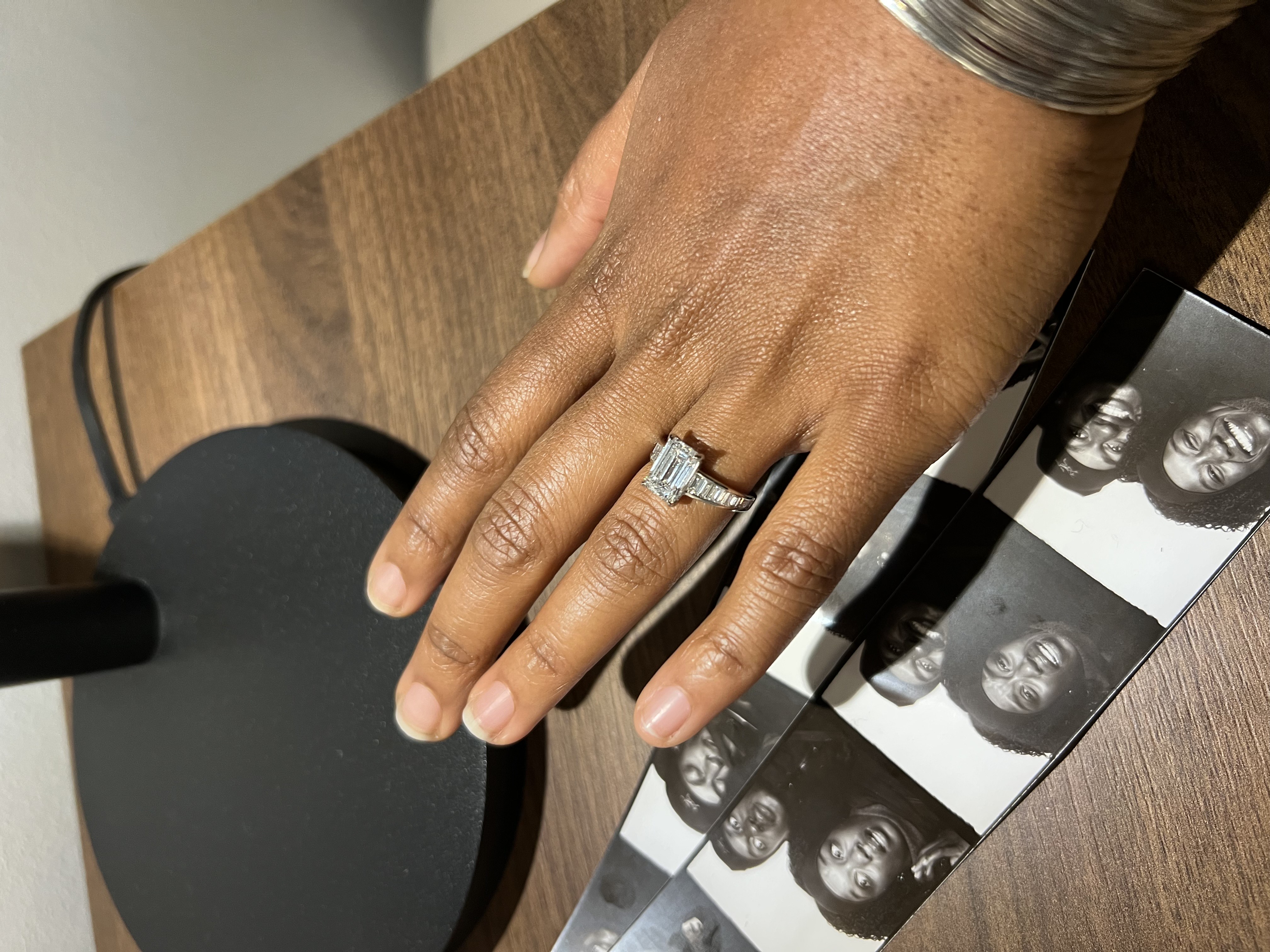 Custom three-stone emerald cut engagement ring on hand next to photo booth pictures of the couple, designed at Haejin Jewelry Brooklyn