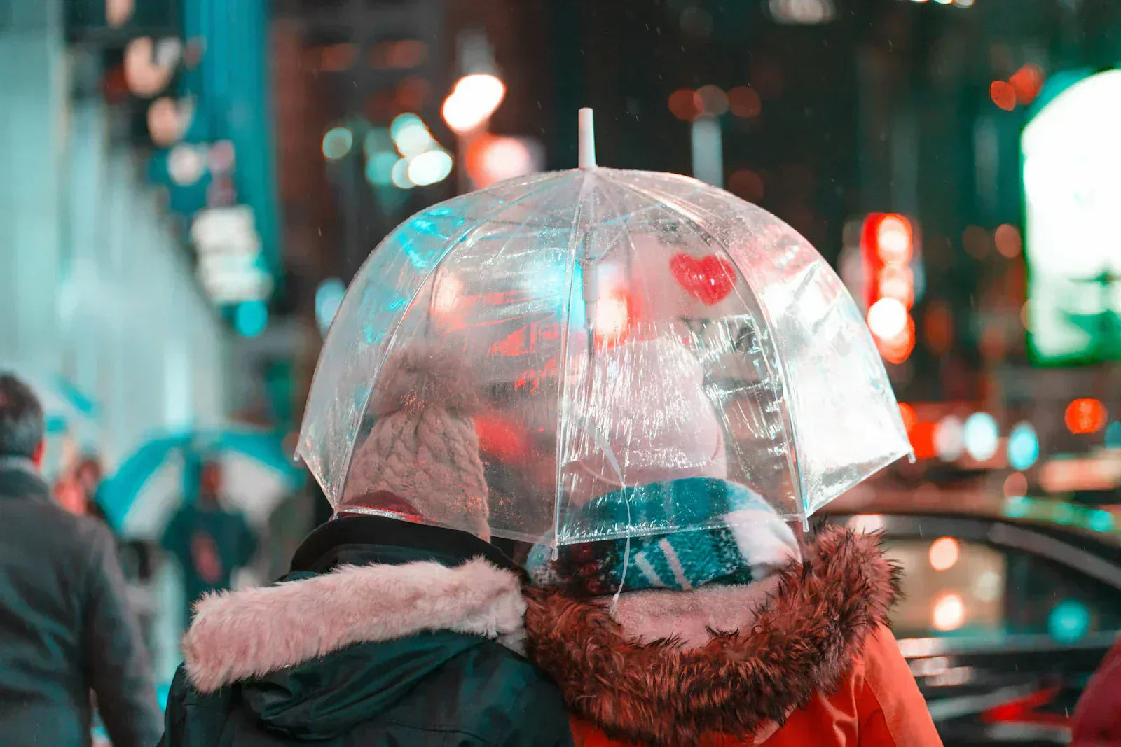 NYC couple walking together under a clear umbrella in glowing city lights, symbolizing love, calm decision-making, and beginning their engagement ring journey in Williamsburg at Haejin Jewelry.